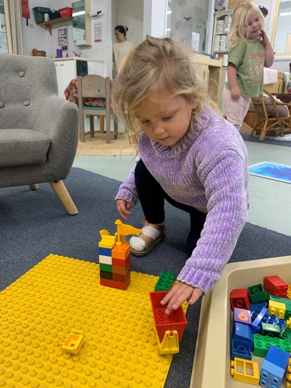 A little girl in a purple sweater is playing with Lego blocks.