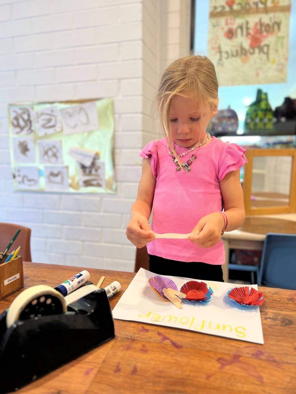 A little girl in a pink shirt is sitting at a table