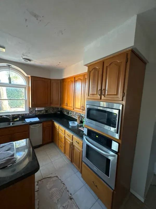 A kitchen with wooden cabinets, dark countertops, a double wall oven, and a large arched window.