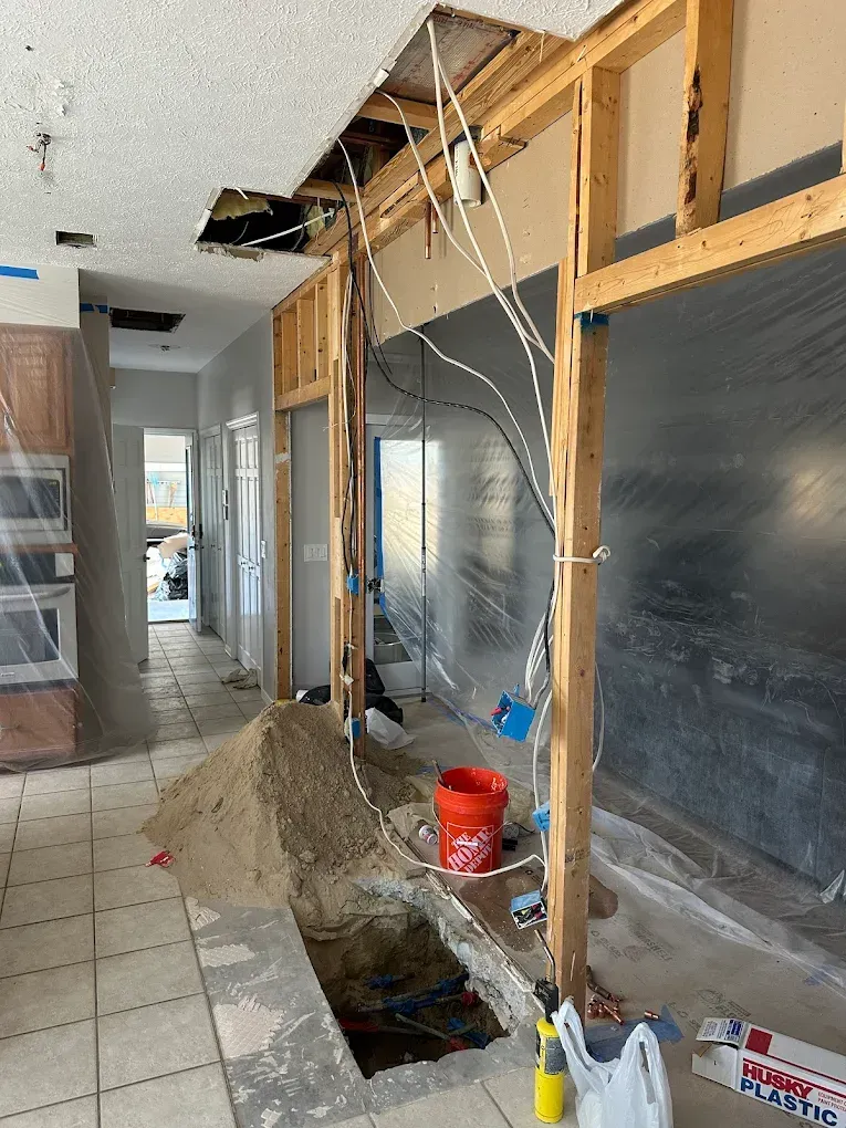 Interior construction site featuring a wooden wall frame, exposed wiring, a hole in the tiled floor, and a pile of dirt.