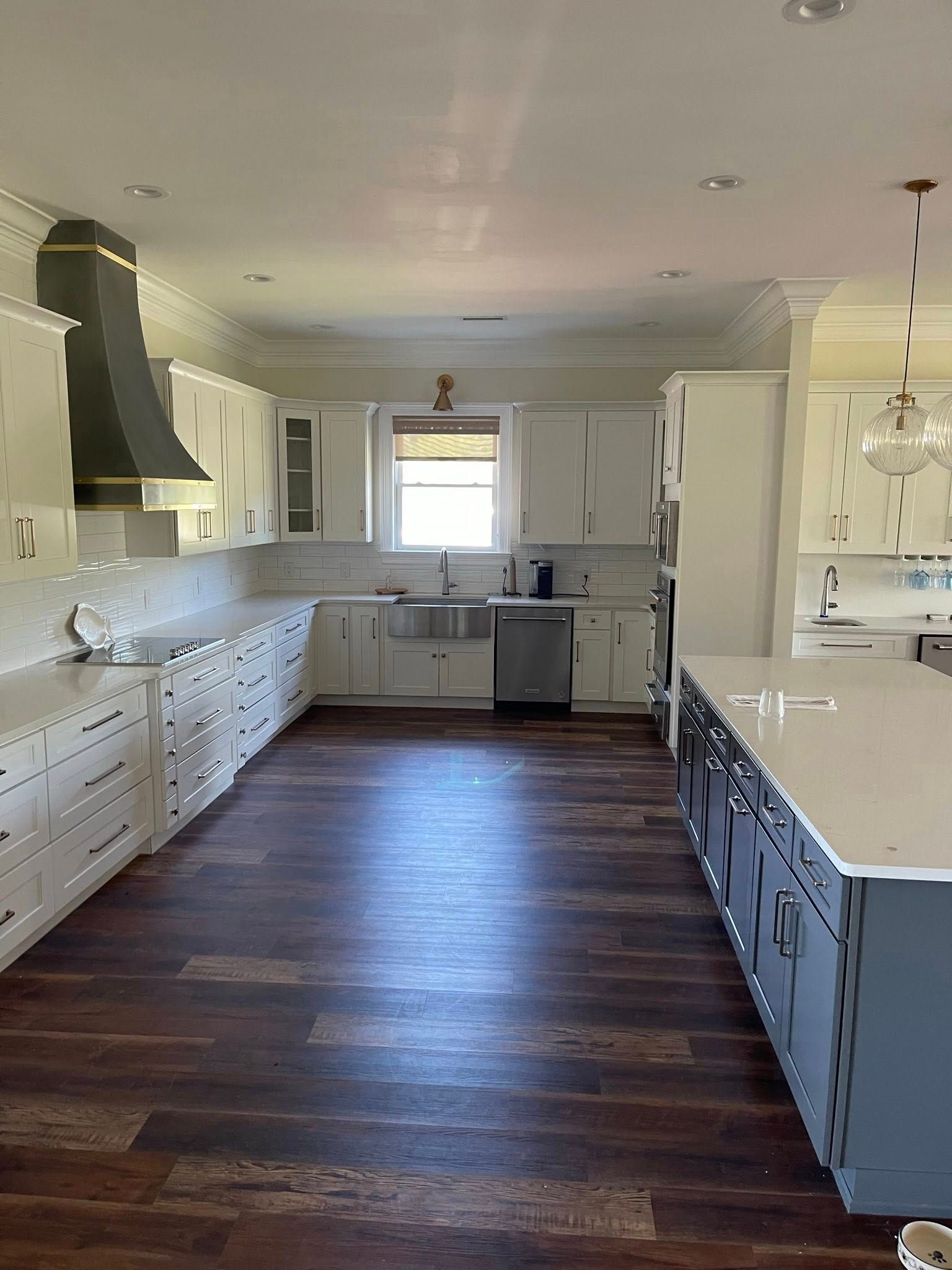 A spacious, modern kitchen featuring white cabinets, a large dark island, dark wood floors, and a dark range hood.