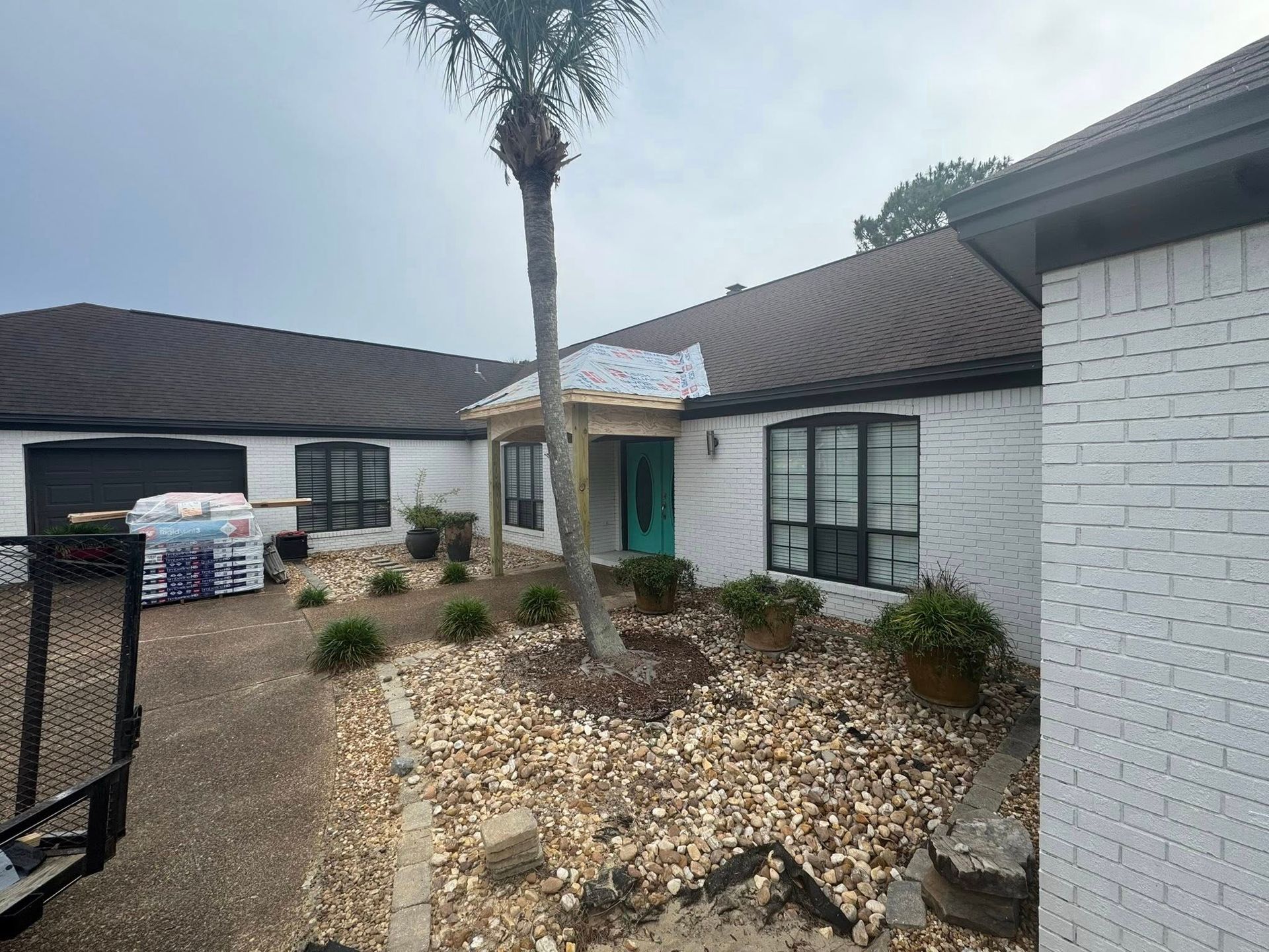 A white brick house exterior featuring a palm tree in the front yard and a small entryway under construction.