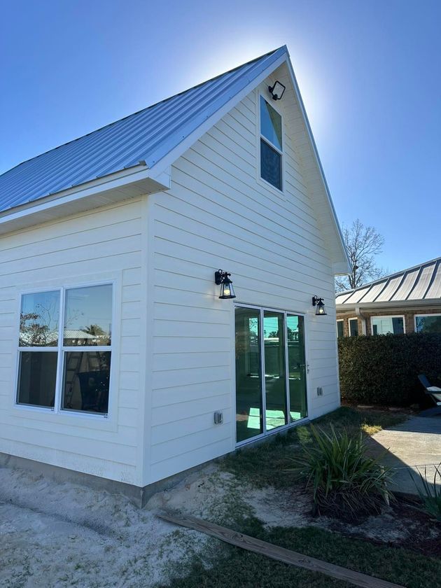 A side view of a white, modern farmhouse with a metal roof, sliding glass doors, and two black exterior wall lamps.