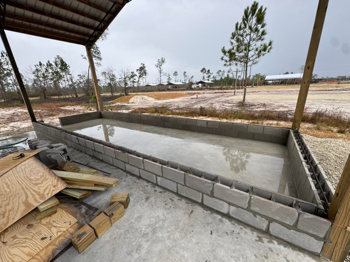 A rectangular concrete foundation structure with cinder block walls, partially filled with water under a wooden shelter.