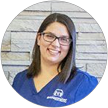 Woman in blue scrubs and glasses smiles in front of a brick wall.
