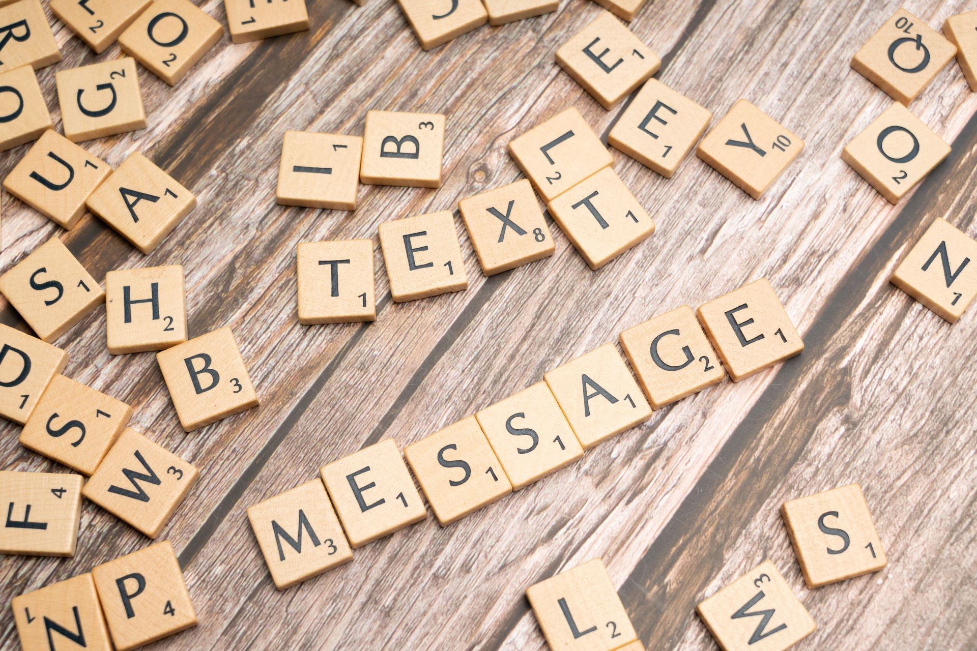 Wooden letter tiles spelling “MESSAGE” on a rustic table, with scattered letters around them.