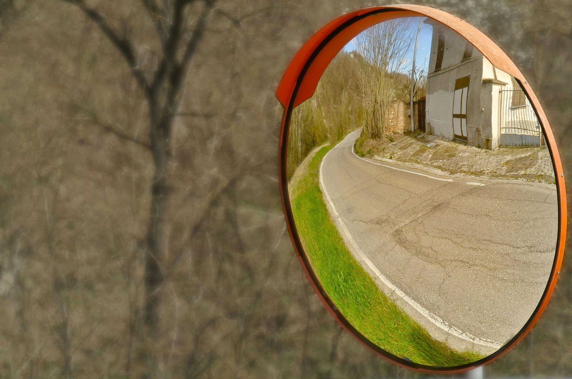 Convex traffic mirror reflecting a curving gravel road beside a house and grassy verge