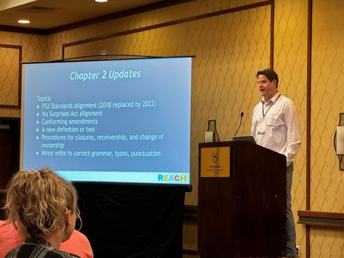 Man presenting at a conference, screen displays