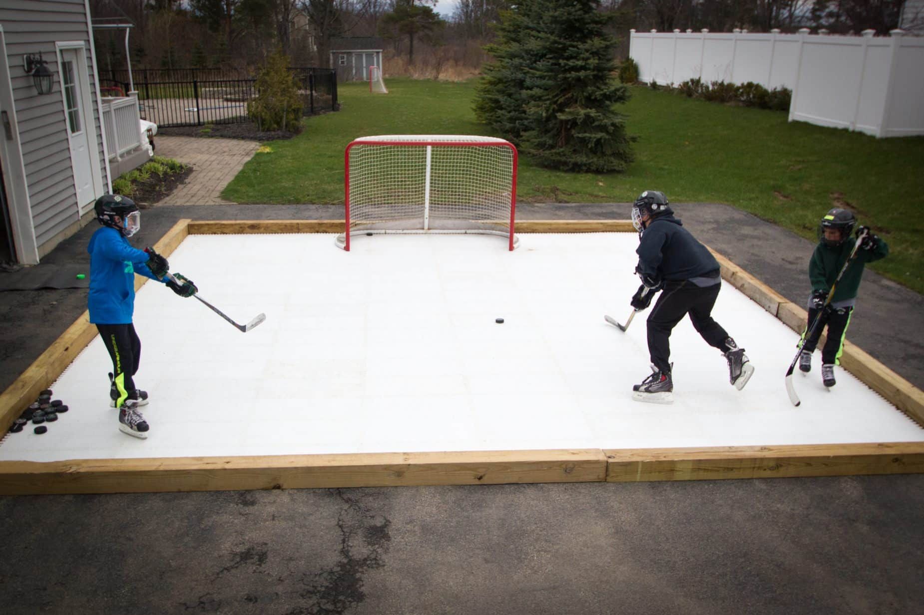 Three people playing hockey on a backyard outdoor rink with a red goal net