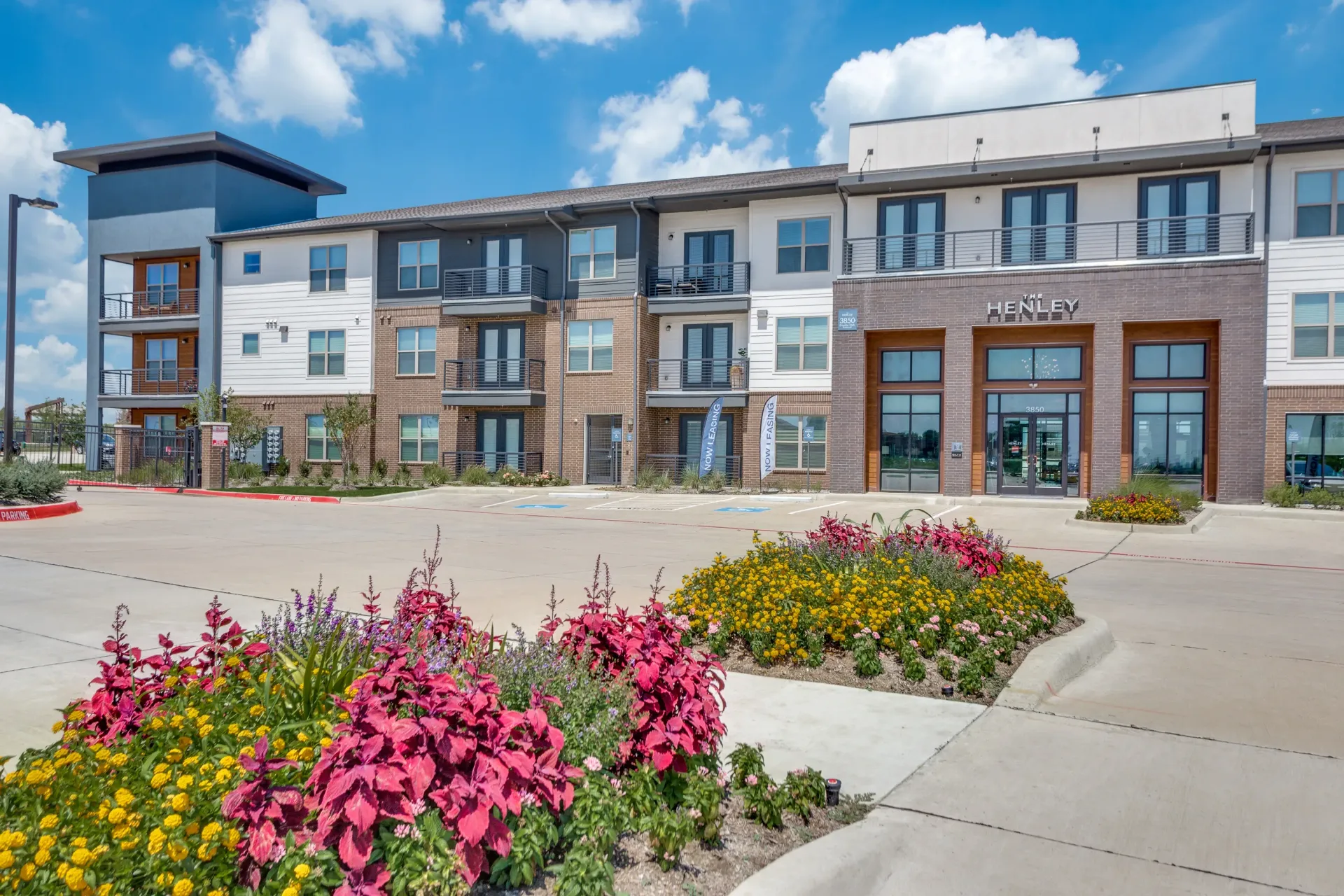 Exterior view of The Henley apartment building with colorful flowers in the foreground.
