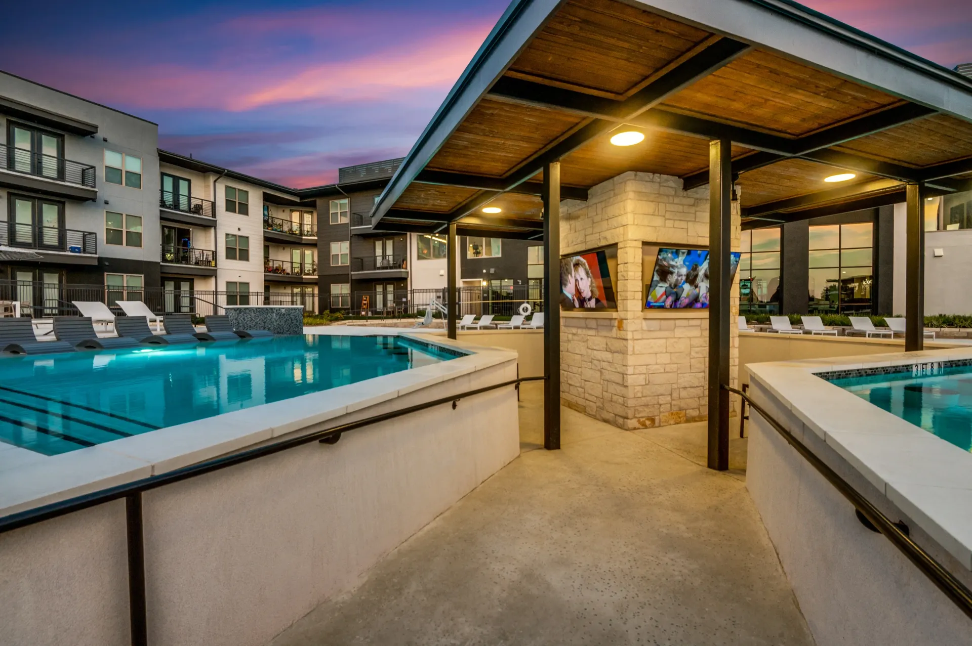 Modern apartment complex with a swimming pool and outdoor entertainment area at dusk.