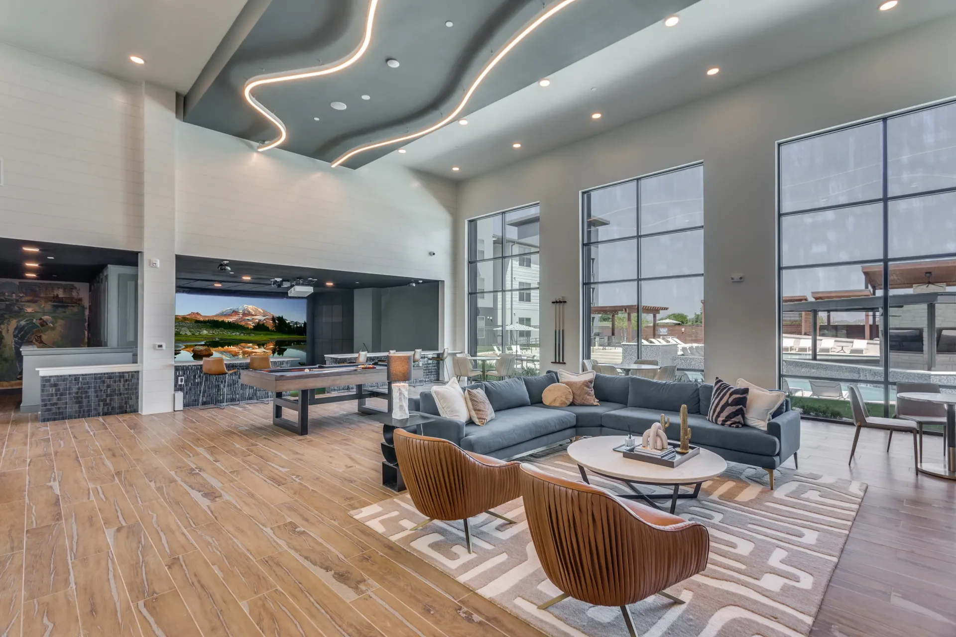 Modern clubhouse lounge with sectional sofa, pool table, and bar area.