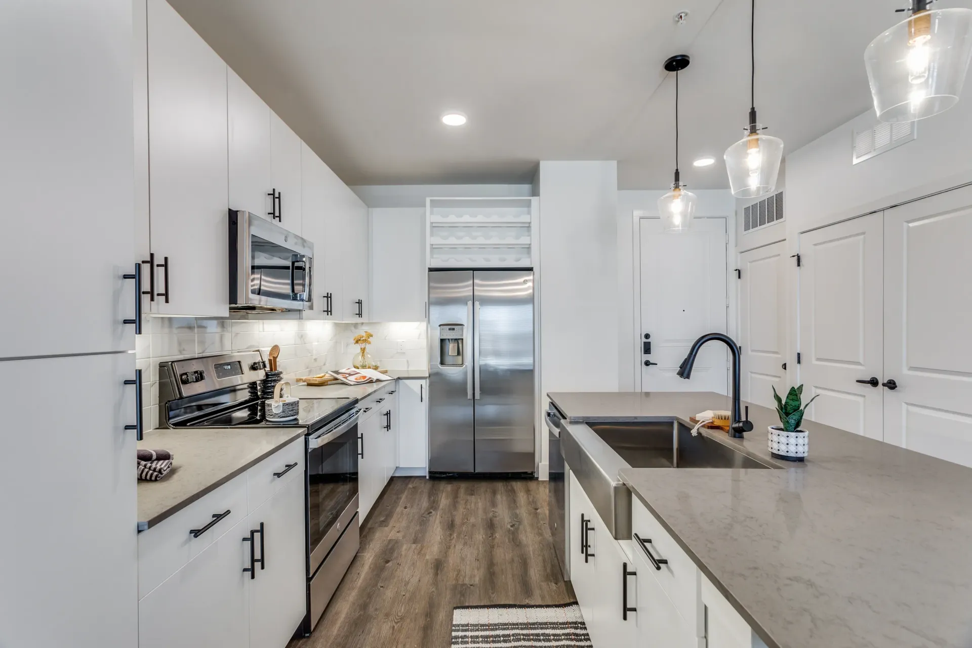 Modern kitchen with stainless steel appliances, white cabinets, and a large island sink.