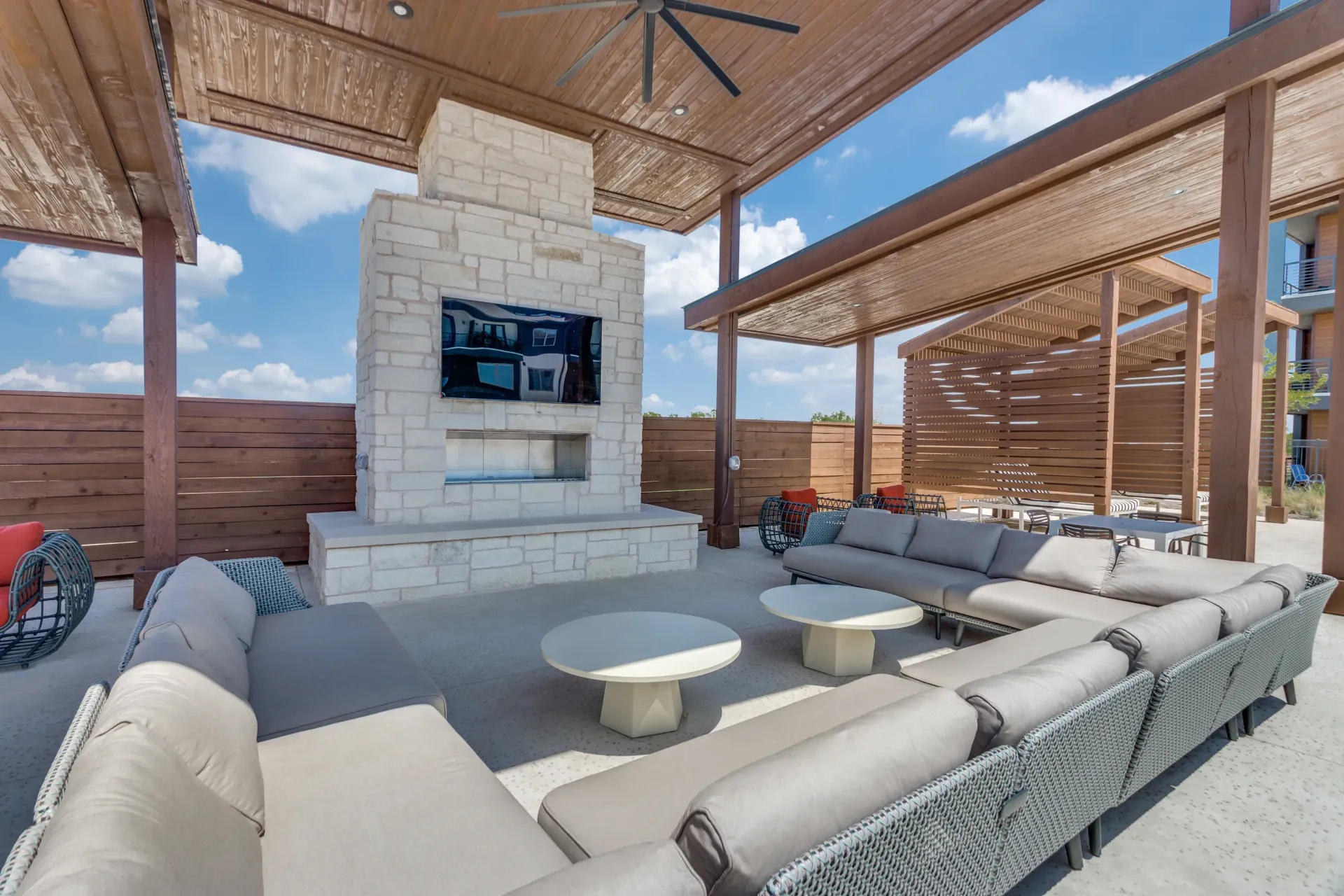 Outdoor lounge area with a stone fireplace, TV, and comfortable seating.