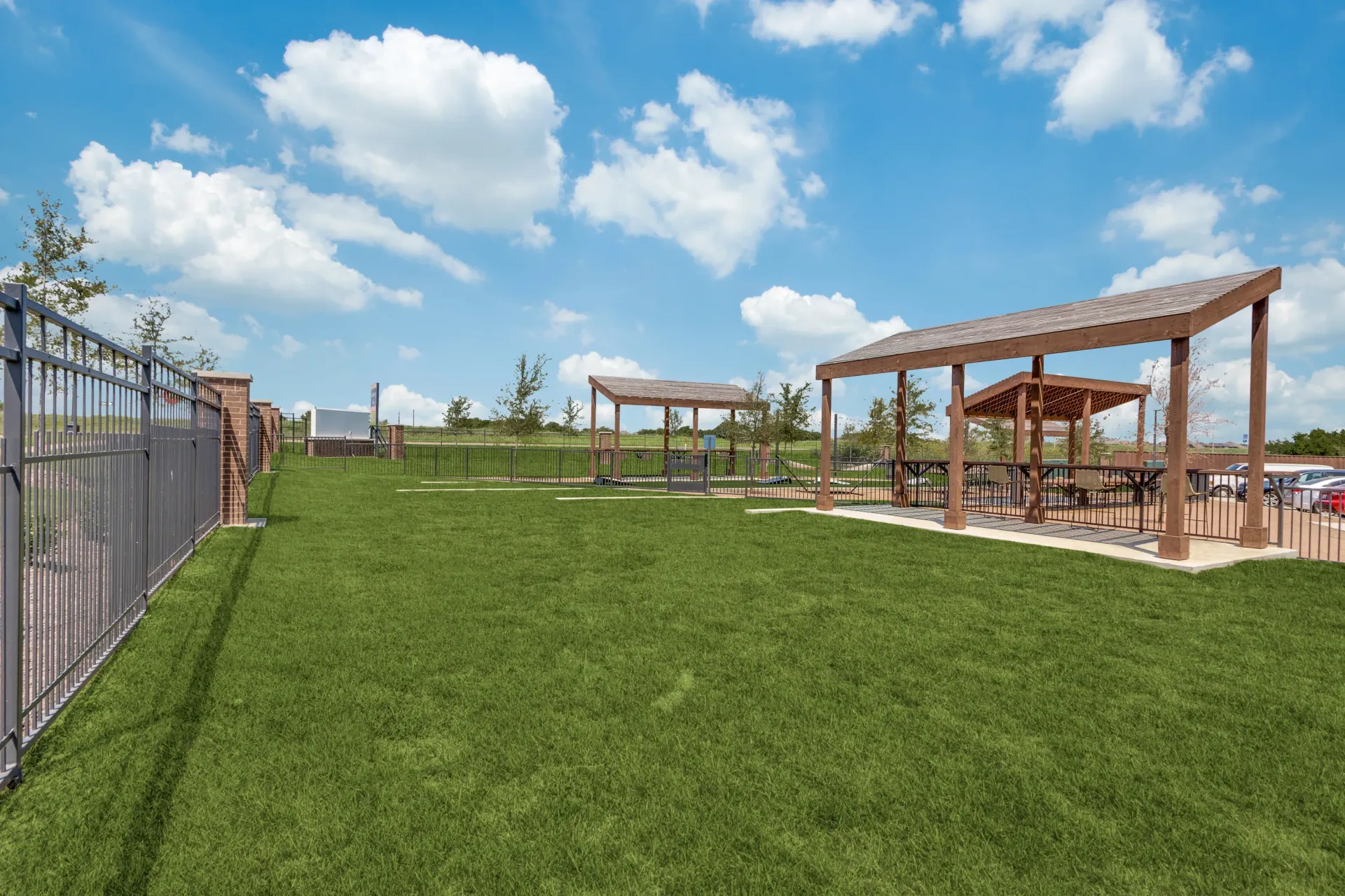Outdoor dog park with fenced areas, benches, and shaded picnic tables.