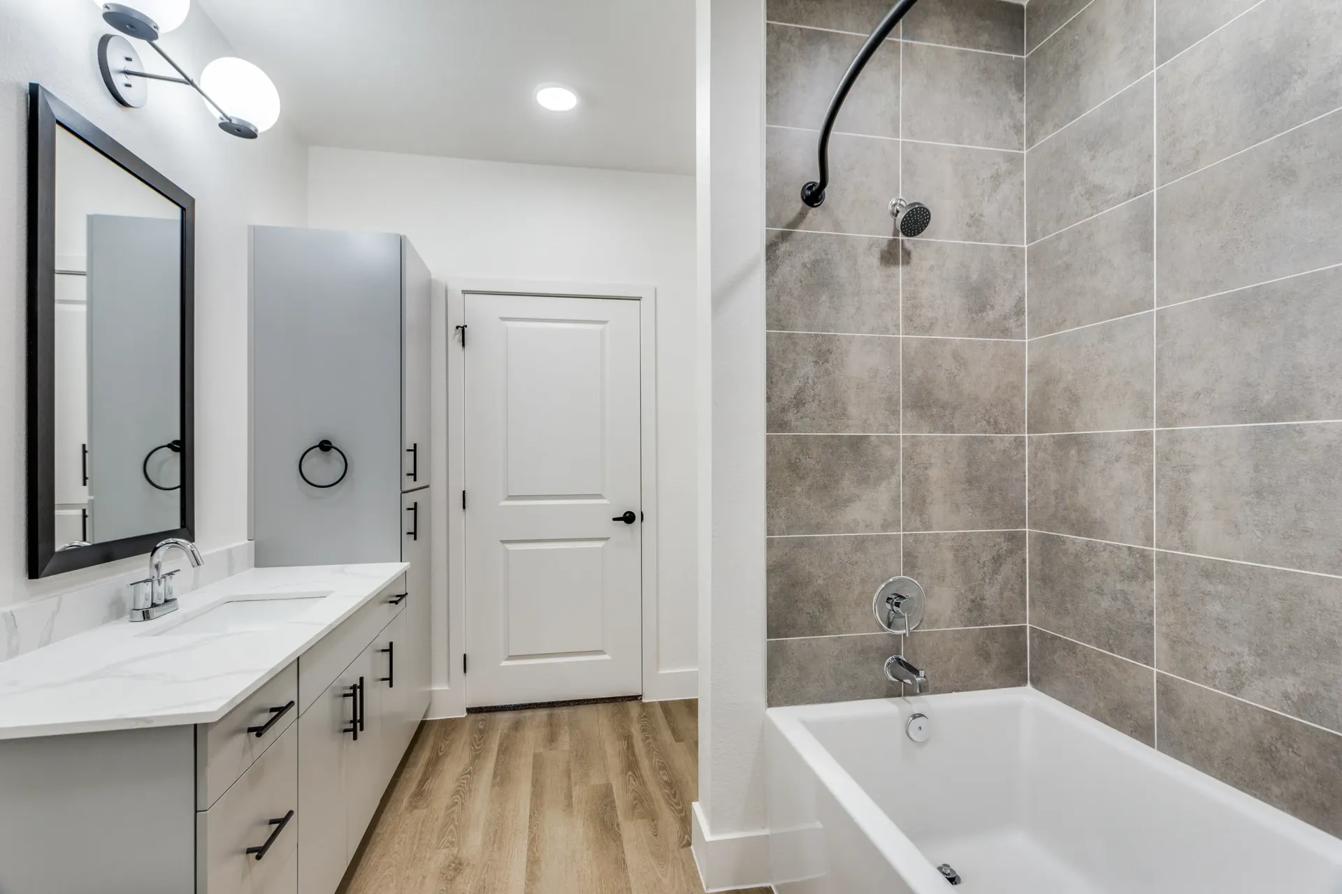 Modern bathroom with a dual vanity, large mirror, and a bathtub with a tiled shower wall.