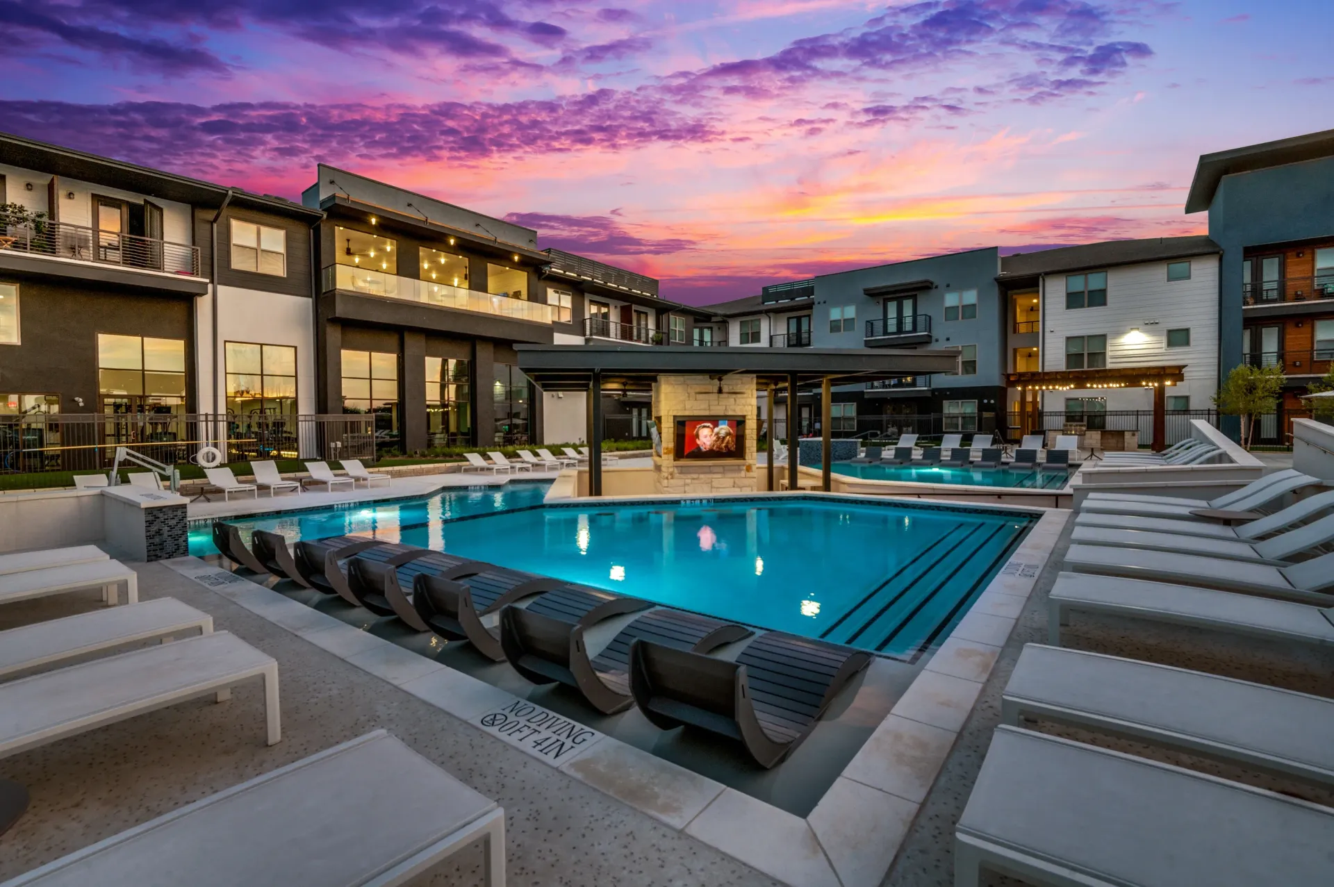Luxury apartment complex with an outdoor swimming pool and lounge chairs at sunset.