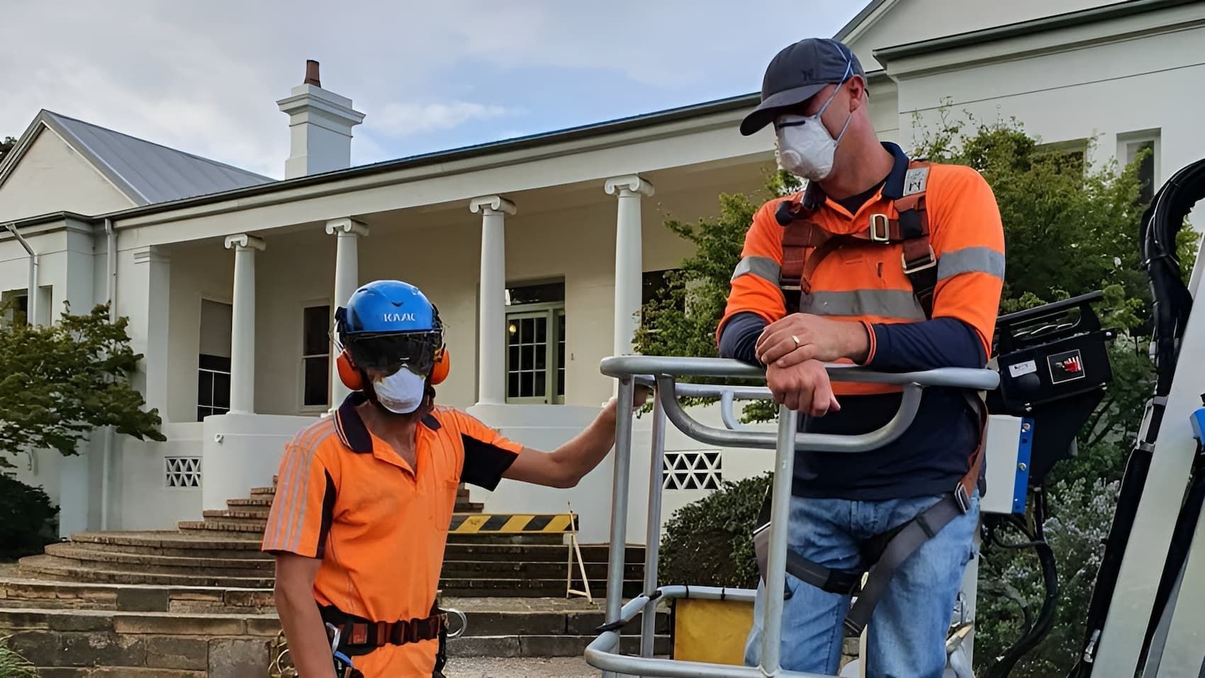 A Man Wearing a Mask Is Standing Next to Another Man Wearing a Mask — Burnett Trees in Kiama, NSW
