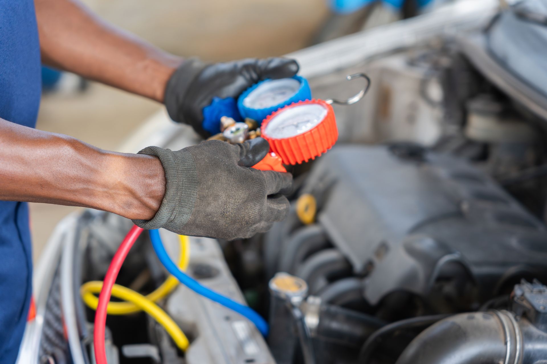 Mechanic using colored hoses and a gauge to service a car engine