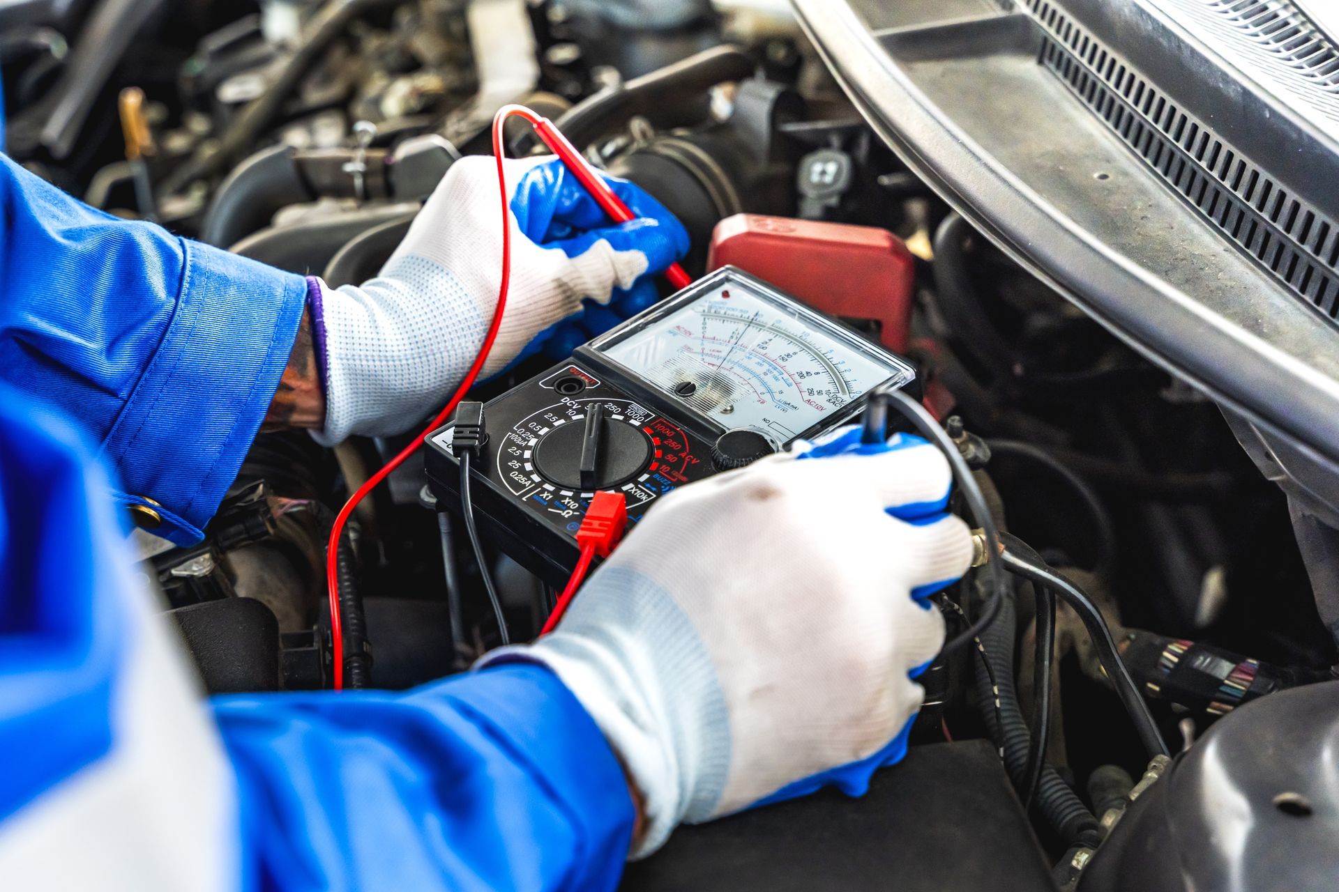 Mechanic testing a car battery with red and black cables in an engine bay