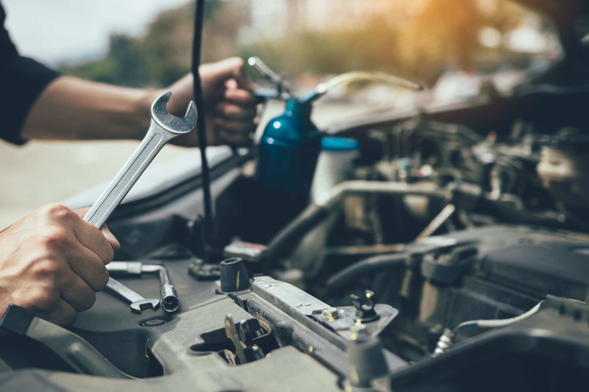Mechanic working under a car hood with tools in an auto repair shop