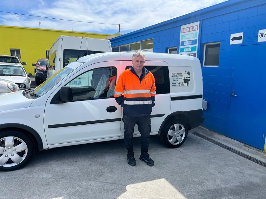 Man in orange hi-vis jacket standing beside a white van in an industrial lot