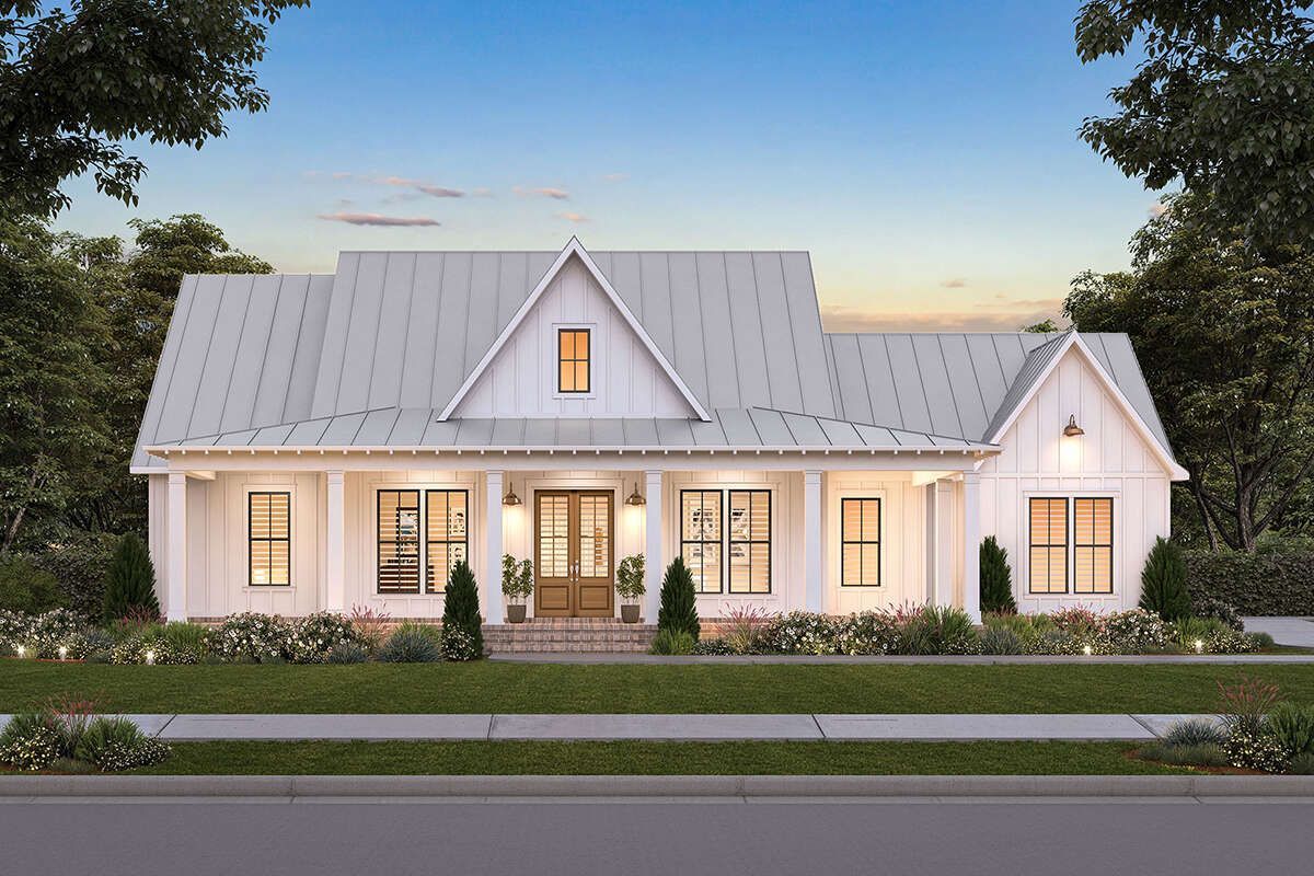 A white house with a metal roof is sitting on top of a lush green lawn.