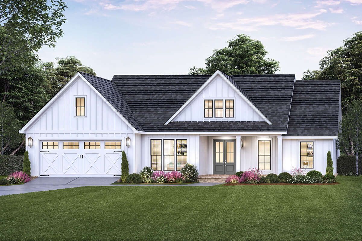 A white house with a black roof is sitting on top of a lush green lawn.
