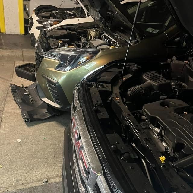 Two severely damaged cars with open hoods in a garage after a collision