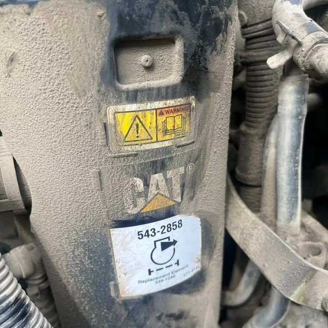 Close-up of a dusty CAT machine panel with warning labels and a white service sticker.
