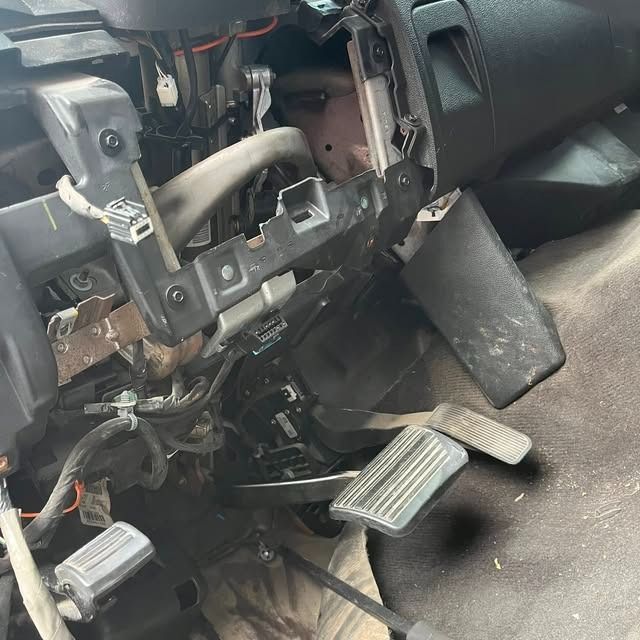 Damaged car dashboard with exposed wiring and detached pedals on the driver’s side.