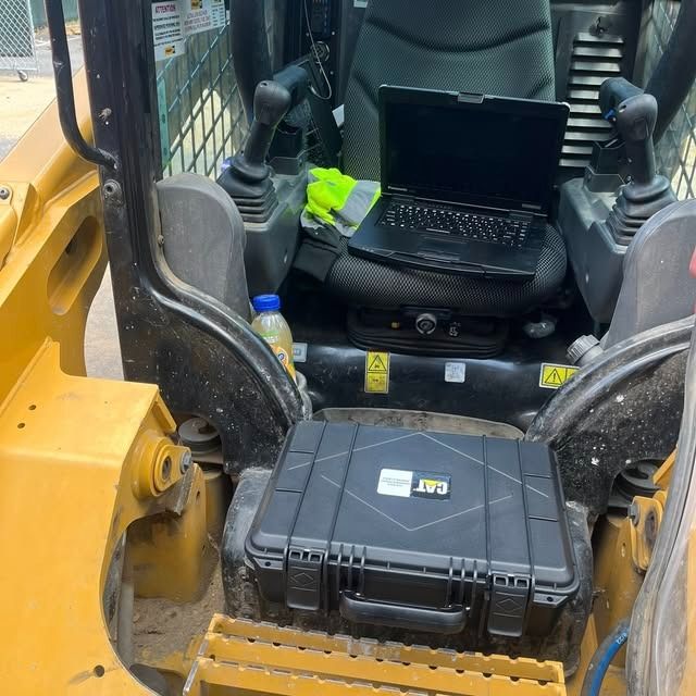 Interior of a yellow construction vehicle cab with a black laptop on the seat and a toolbox on the floor