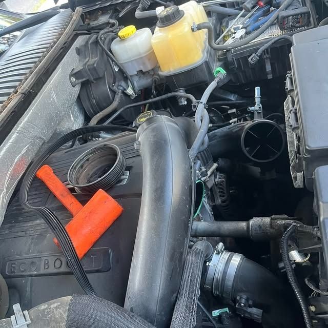 Open car engine bay with a black intake tube, orange clamp, and coolant reservoir visible