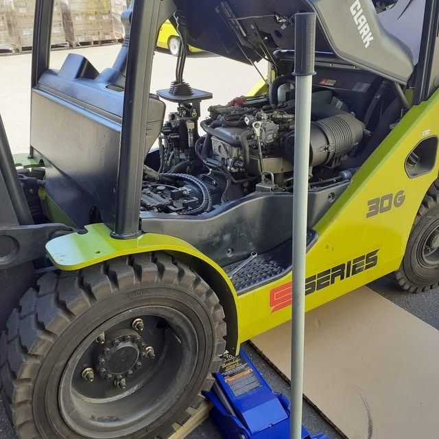 Yellow forklift truck in a garage bay with its front wheel lifted on a blue jack.