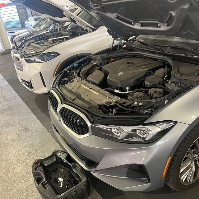 Silver car with hood open in a garage, engine exposed, another car behind it and a tool case on the floor