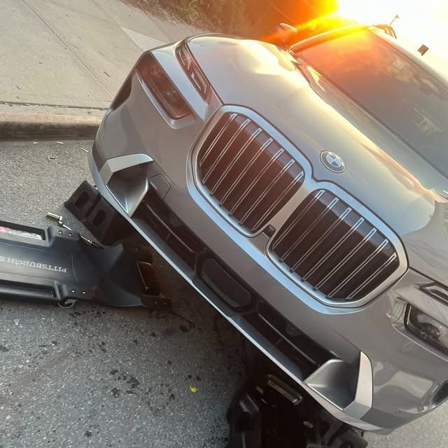 Silver BMW SUV crashed onto a curb with front-end damage and flashing hazard lights
