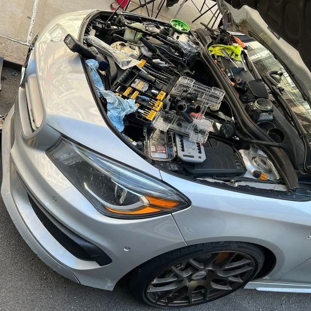 Silver car with front end open, engine exposed, parked in a garage or repair bay