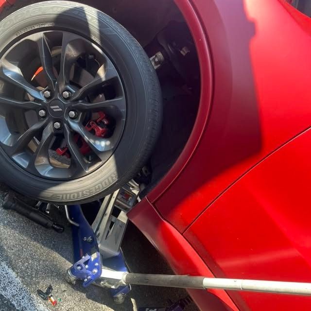 Red sports car lifted by a jack, with a detached wheel and brake visible in a garage.