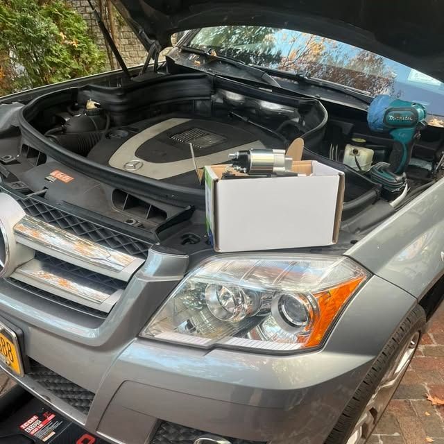 Silver SUV with open hood and a box of tools in the engine bay, parked outdoors on a driveway.
