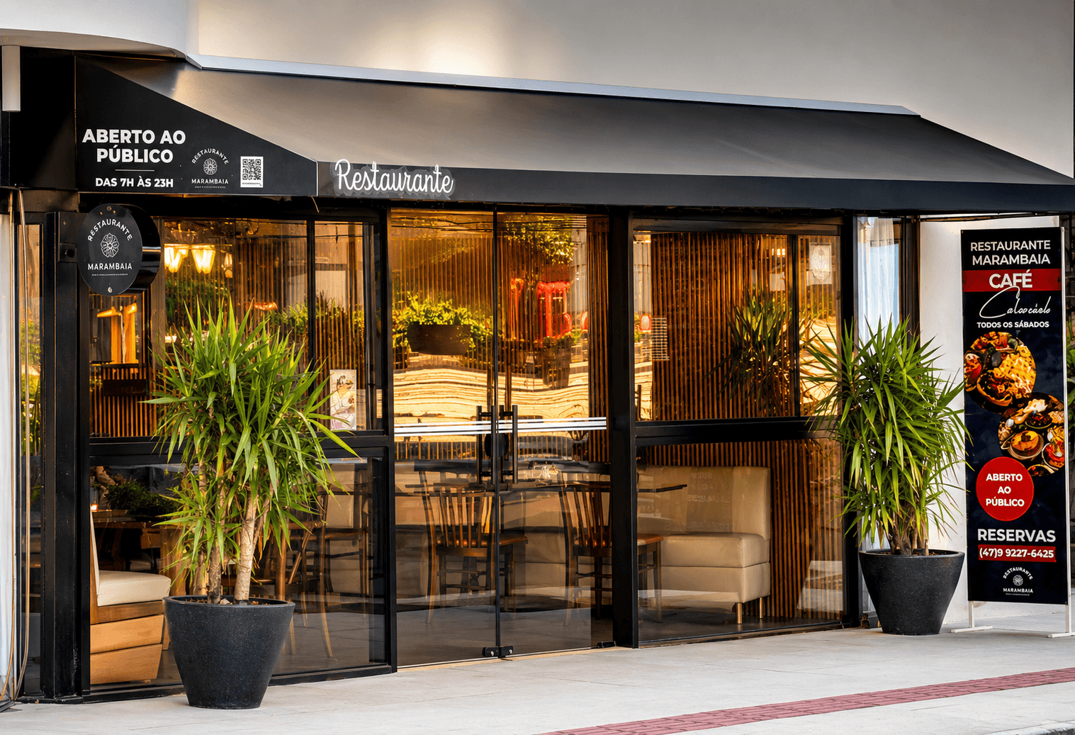 Fachada de restaurante com toldo preto, entrada de vidro e vasos de plantas na porta.