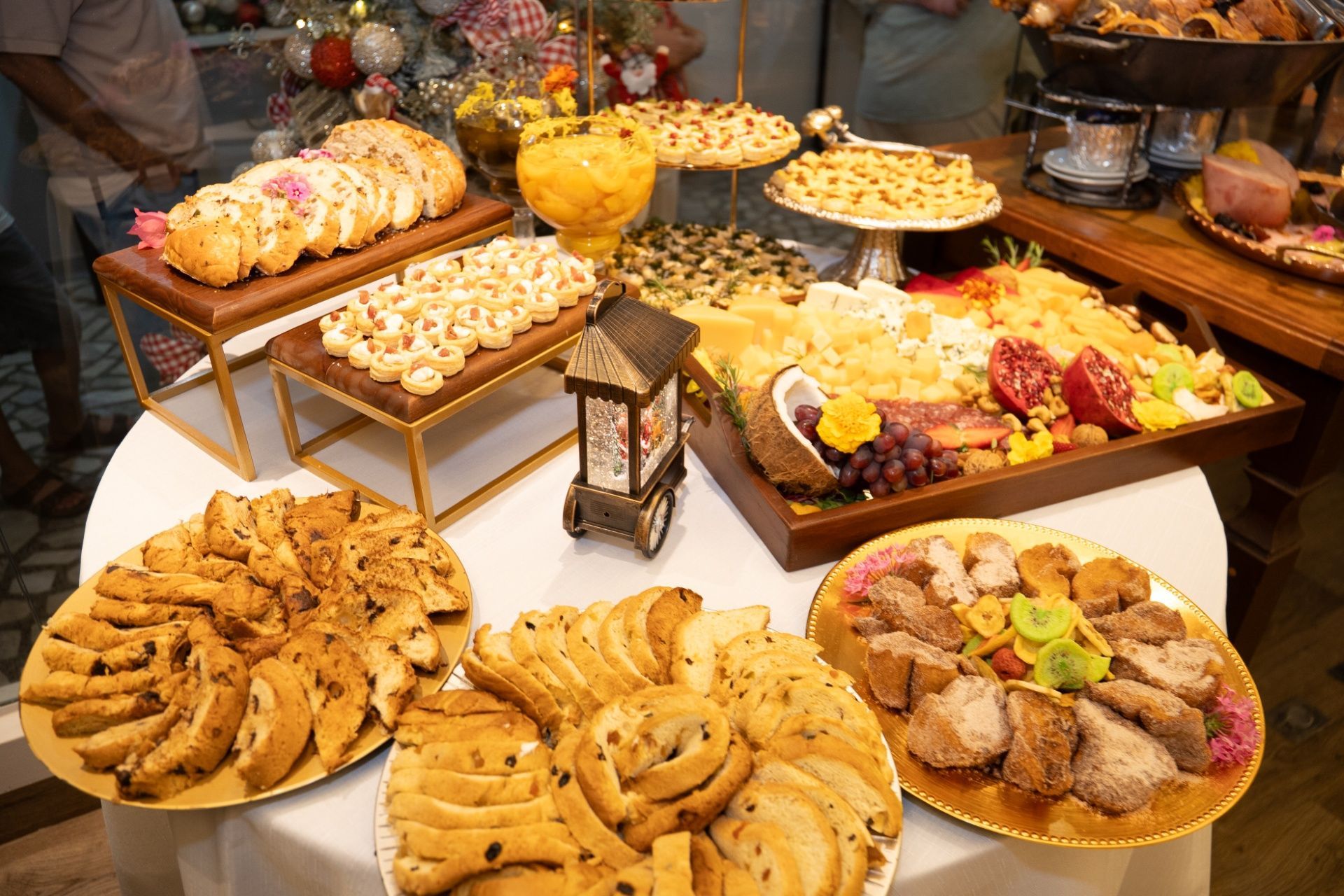 Buffet servido em mesas compridas em uma sala de jantar moderna com paredes de vidro e plantas.