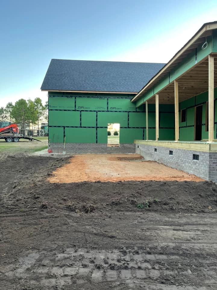 Partially built green building with a dirt foreground and covered porch under construction.