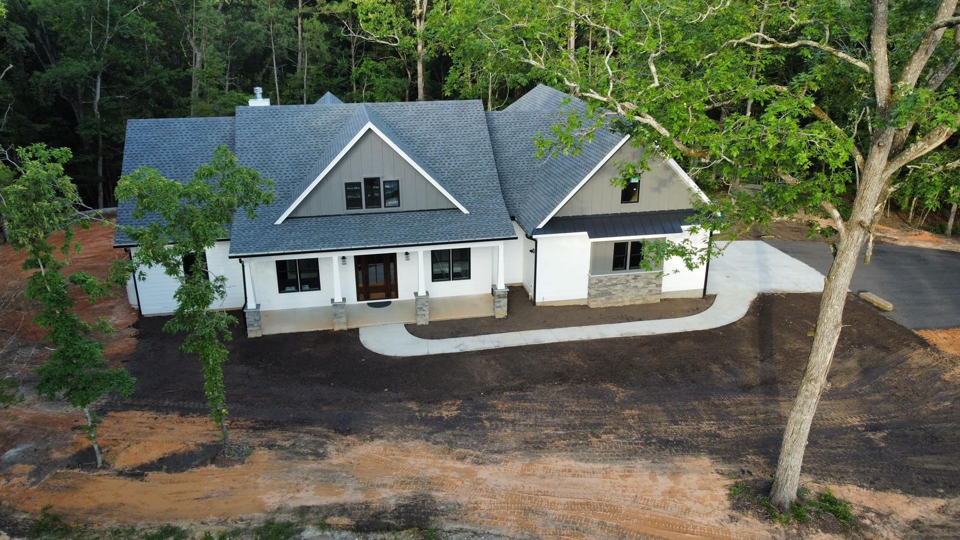 Small white house with gray roof and front porch, surrounded by trees and bare dirt yard.