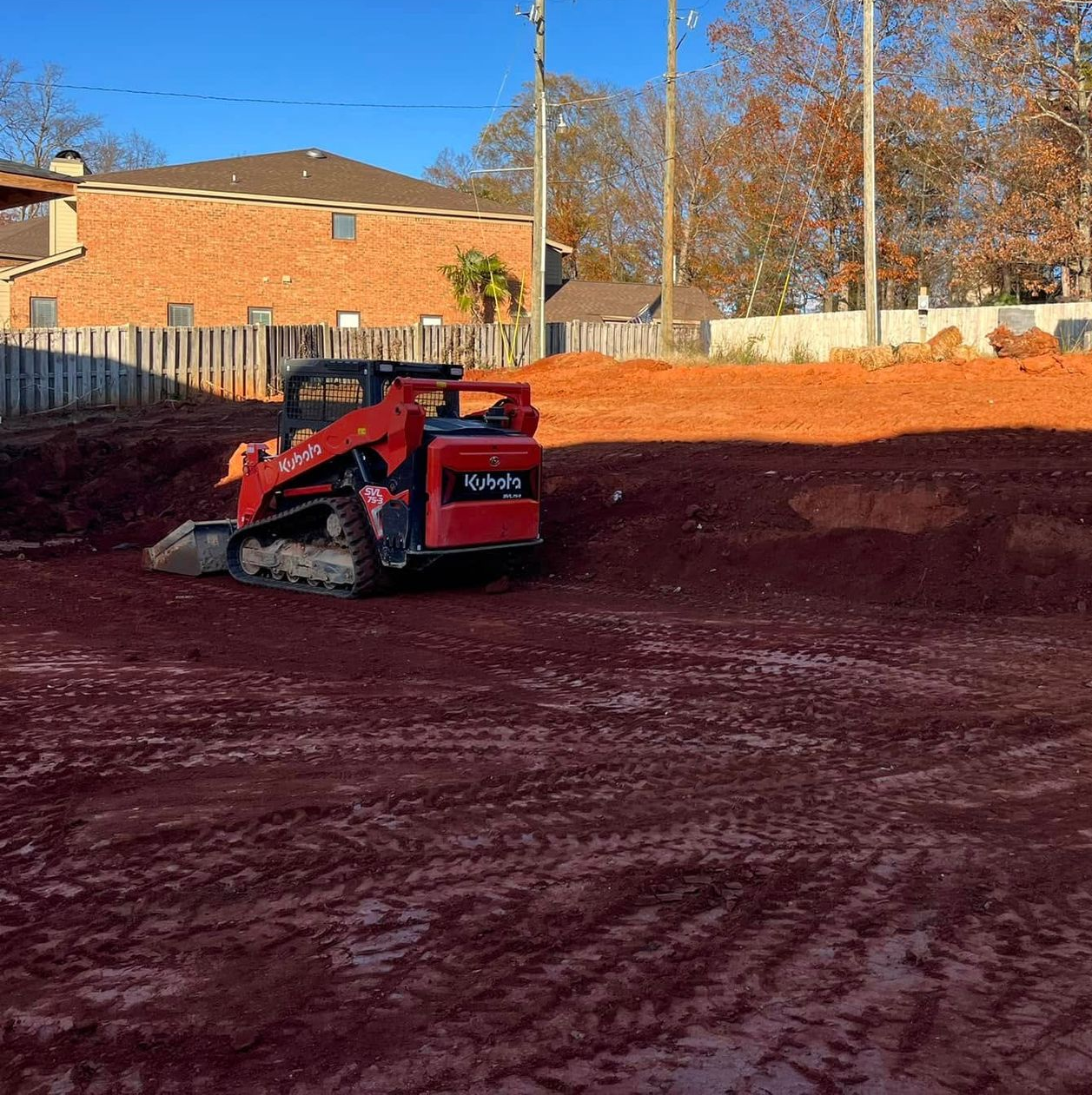 Red compact skid steer leveling red dirt on a construction site at sunset