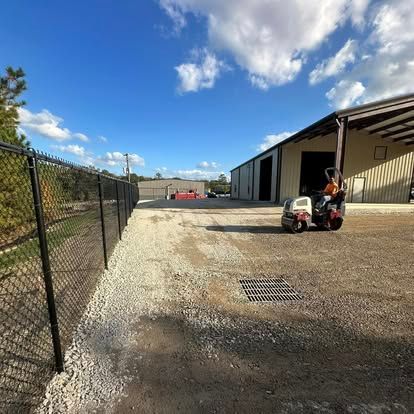 Industrial yard with gravel drive, chain-link fence, and worker on a small utility vehicle beside a warehouse