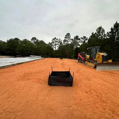 Construction site with orange dirt, a bulldozer, and a silt fence under an overcast sky