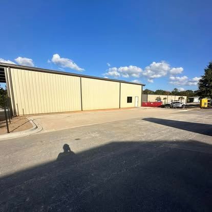 Wide beige metal warehouse with a paved lot under a bright blue sky and scattered clouds