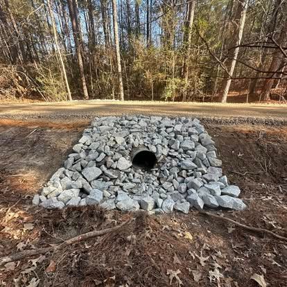 Rock-lined culvert pipe under a dirt road beside leafless woods