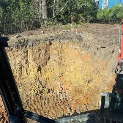 Excavator view of a large dirt excavation pit with exposed yellow soil and trees in the background