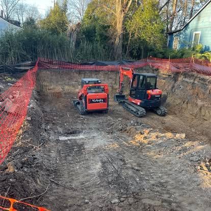 Two orange excavators on a dirt construction site surrounded by orange safety fencing and trees.